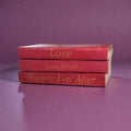 Stack of red books with gold text, love, laughter, and happily ever after, on a purple background